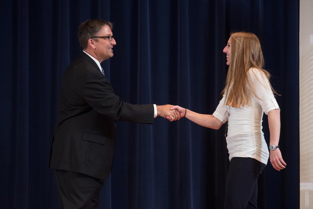 Doctor Smart shaking hands with an award recipient in a long sleeved white shirt